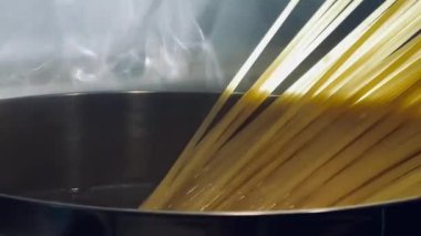 Altın renkli spagetti telleri, sıcak ve sade bir yemeğin başlangıcını yakalayan, kaynayan bir su kabına nazikçe eklenir.