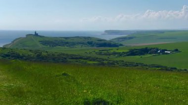 Eastbourne yakınlarındaki İngiliz kırsalında, Doğu Sussex, Birleşik Krallık, sakin kıyı şeridine karışan yemyeşil alanlar ve parlak bir gökyüzü altında sakin mavi deniz