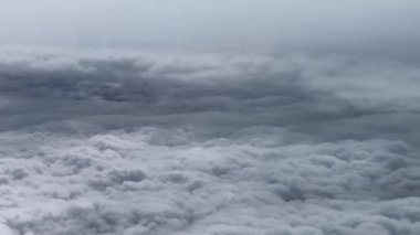 Bulutların üzerine bak, yumuşak katmanlı, dalgalı gri gökyüzünün altında dalgalanan desenlerle beyaz oluşumlardan oluşan bir denizi göster.