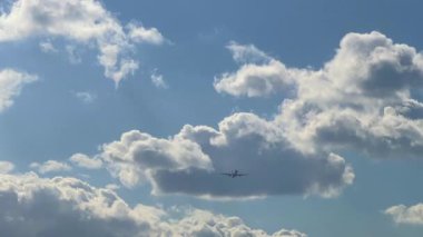 Parlak mavi bir gökyüzü, dağınık beyaz bulutlar ve uzaktan görülebilen bir uçak bulutların altında uçuyor, özgürlük hissi yaratıyor ve açık gökyüzüne karşı seyahat ediyor.