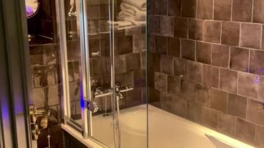 Koyu fayanslı duvarları, krom aksesuarları ve modern İngiliz tasarım fikrinde cam panelli banyosu olan şık bir Londra otel banyosu.