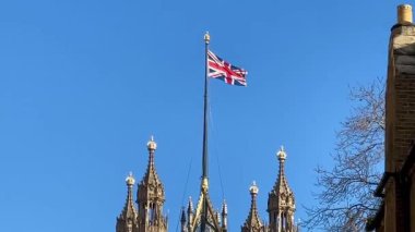 İngiliz bayrağı, Westminster, Londra 'daki açık mavi gökyüzünün altında Parlamento Binaları' nın detaylı bir kulesinde dalgalanıyor.