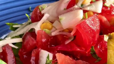 Canlı, mavi bir kasede servis edilen domates, soğan, marul ve limon dilimlerinden oluşan taze bir Akdeniz salatası..