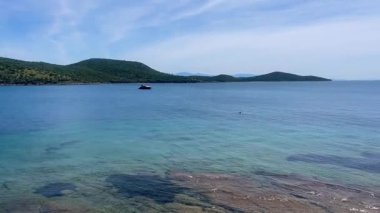Türkiye 'nin Bodrum kenti yakınlarındaki yeşil tepelere doğru uzanan berrak turkuaz deniz suyu, sakin sahile doğru hafif dalgalarla ağır çekimde ilerliyor.