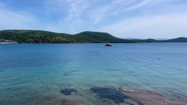 Türkiye 'nin Bodrum kenti yakınlarındaki yeşil tepelere doğru uzanan berrak turkuaz deniz suyu, sakin sahile doğru hafif dalgalarla ağır çekimde ilerliyor.