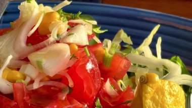 Canlı, mavi bir kasede servis edilen domates, soğan, marul ve limon dilimlerinden oluşan taze bir Akdeniz salatası..
