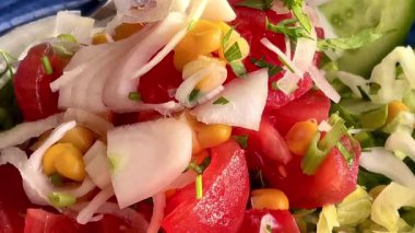 Canlı, mavi bir kasede servis edilen domates, soğan, marul ve limon dilimlerinden oluşan taze bir Akdeniz salatası..