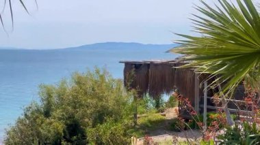 Palmiyeler ve çalılar arasında yuva yapmış kıyı kulübesi Türkiye 'nin Bodrum kenti yakınlarındaki sakin Ege sularına bakıyor..