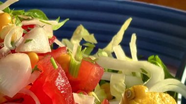 Canlı, mavi bir kasede servis edilen domates, soğan, marul ve limon dilimlerinden oluşan taze bir Akdeniz salatası..