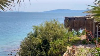 Palmiyeler ve çalılar arasında yuva yapmış kıyı kulübesi Türkiye 'nin Bodrum kenti yakınlarındaki sakin Ege sularına bakıyor..