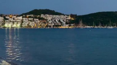 Durgun akşam ışığı, Türkiye 'nin Bodrum kenti yakınlarındaki kıyı şeridine yansıyor. Körfez boyunca parlayan sessiz dalgalar ve yamaçtaki evler, ağır çekimde..