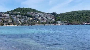 Parlak turkuaz deniz suları, açık bir yaz gökyüzü altında Türkiye 'nin Bodrum kenti yakınlarında yeşil tepelerle ve beyazlatılmış evlerle buluşuyor..