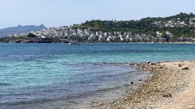 Açık turkuaz deniz suları Türkiye 'nin Bodrum kenti yakınlarındaki çakıl taşlı kıyılarda yeşil tepeler ve uzakta beyaz evler ile nazikçe buluşuyor.
