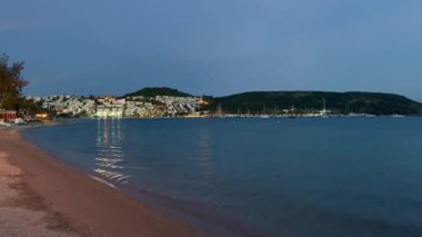 Durgun akşam ışığı, Türkiye 'nin Bodrum kenti yakınlarındaki kıyı şeridine yansıyor. Körfez boyunca parlayan sessiz dalgalar ve yamaçtaki evler, ağır çekimde..