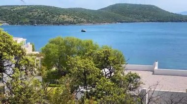 Türkiye 'nin Bodrum kenti yakınlarındaki derin mavi deniz ve tepelere doğru yeşil ağaçların tepelerini ve beyazlatılmış çatıları izliyorlar..