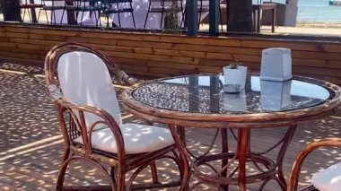 Türkiye 'nin Bodrum kentindeki ahşap bir gölgeliğin altında, portatif sandalyeli ve cam kapaklı bir kafeterya masası.