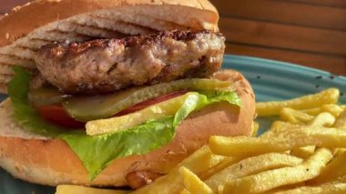 Marul, domates ve turşulu ızgara burger, deniz kenarındaki bir restoranda turkuaz bir tabakta altın cipsle servis edilir.