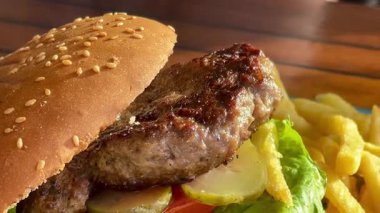 Marul, domates ve turşulu ızgara burger, deniz kenarındaki bir restoranda turkuaz bir tabakta altın cipsle servis edilir.