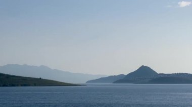 Türkiye 'nin Bodrum kenti yakınlarındaki mavi deniz, katmanlı tepeler açık bir sabah gökyüzü altında yavaş çekim kayboluyor.