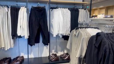 Akıllı gömlekler ve klasik tonda pantolonlar erkek giyim mağazasında ahşap bir duvara, hızlı moda konseptine, yavaş çekim fikrine karşı düzgünce asılıdır.