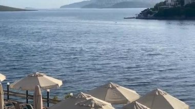 Şemsiyeler ve dinlenme yerleri, Türkiye 'nin Bodrum kenti yakınlarında sakin mavi dalgalara, yavaş çekime bakan huzurlu bir rıhtımda kuyruk oluşturuyorlar.