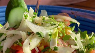 Canlı, mavi bir kasede servis edilen domates, soğan, marul ve limon dilimlerinden oluşan taze bir Akdeniz salatası..