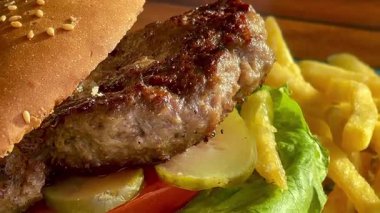 Marul, domates ve turşulu ızgara burger, deniz kenarındaki bir restoranda turkuaz bir tabakta altın cipsle servis edilir.