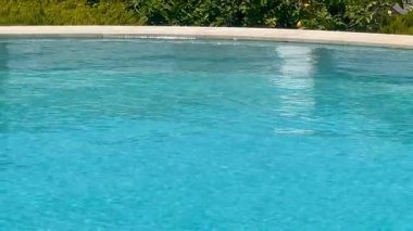 Turkuaz yüzme havuzu öğle sıcağı altında parıldıyor, ağır çekim.