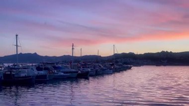 Türkiye 'nin Bodrum kenti yakınlarında, pembe ve lavantalı bir akşam gökyüzünün altında, alacakaranlık sakin sularda yavaş çekimde yansıyor.