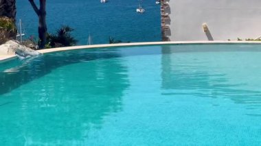 Turkuaz havuzu, Türkiye 'nin Bodrum kenti yakınlarında yavaşça sürüklenen yelkenli tekneleriyle ardındaki parlak denizi yansıtıyor.