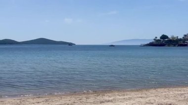 Sakin kumlu bir sahil, Türkiye 'nin Bodrum kenti yakınlarında, yumuşak bir yaz gökyüzü altında sakin mavi sularla buluşuyor.