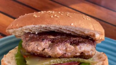 Marul, domates ve turşulu ızgara burger, deniz kenarındaki bir restoranda turkuaz bir tabakta altın cipsle servis edilir.