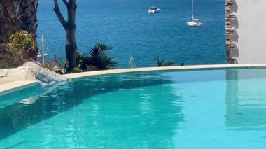 Turkuaz havuzu, Türkiye 'nin Bodrum kenti yakınlarında yavaşça sürüklenen yelkenli tekneleriyle ardındaki parlak denizi yansıtıyor.