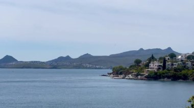 Beyazlatılmış villalar, Türkiye 'nin Bodrum kenti yakınlarındaki sakin Ege Denizi' nin üzerinde kayalık bir yarımadadan öteye yükselen dağlarla birlikte, ağır çekimde ilerliyorlar..