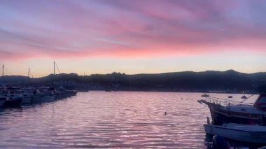 Türkiye 'nin Bodrum kenti yakınlarında, pembe ve lavantalı bir akşam gökyüzünün altında, alacakaranlık sakin sularda yavaş çekimde yansıyor.