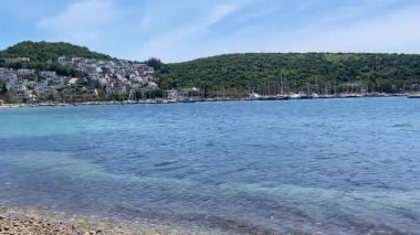Açık turkuaz deniz suları Türkiye 'nin Bodrum kenti yakınlarındaki çakıl taşlı kıyılarda yeşil tepeler ve uzakta beyaz evler ile nazikçe buluşuyor.