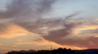 Altın akşam ışığı, Türkiye 'nin Bodrum kentindeki liman ve yamaç kenarındaki evlerin üzerine hafifçe düşüyor. Parlayan bulutların altında demirlemiş tekneler, ağır çekim.