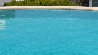 Turkuaz yüzme havuzu öğle sıcağı altında parıldıyor, ağır çekim.