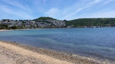 Açık turkuaz deniz suları Türkiye 'nin Bodrum kenti yakınlarındaki çakıl taşlı kıyılarda yeşil tepeler ve uzakta beyaz evler ile nazikçe buluşuyor.