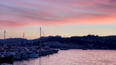 Türkiye 'nin Bodrum kenti yakınlarında, pembe ve lavantalı bir akşam gökyüzünün altında, alacakaranlık sakin sularda yavaş çekimde yansıyor.