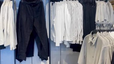 Akıllı gömlekler ve klasik tonda pantolonlar erkek giyim mağazasında ahşap bir duvara, hızlı moda konseptine, yavaş çekim fikrine karşı düzgünce asılıdır.