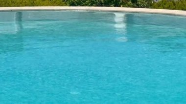 Turkuaz yüzme havuzu öğle sıcağı altında parıldıyor, ağır çekim.