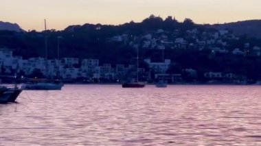 Türkiye 'nin Bodrum kenti yakınlarında, pembe ve lavantalı bir akşam gökyüzünün altında, alacakaranlık sakin sularda yavaş çekimde yansıyor.