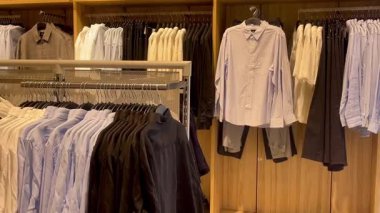 Akıllı gömlekler ve klasik tonda pantolonlar erkek giyim mağazasında ahşap bir duvara, hızlı moda konseptine, yavaş çekim fikrine karşı düzgünce asılıdır.