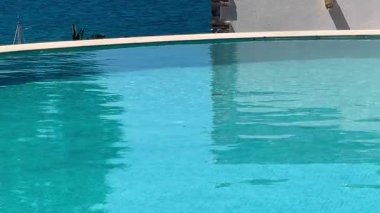 Turkuaz havuzu, Türkiye 'nin Bodrum kenti yakınlarında yavaşça sürüklenen yelkenli tekneleriyle ardındaki parlak denizi yansıtıyor.