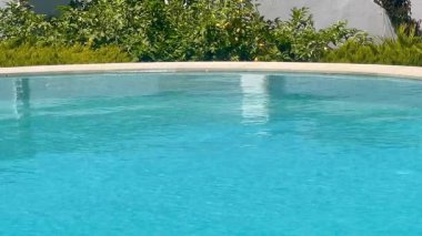 Turkuaz yüzme havuzu öğle sıcağı altında parıldıyor, ağır çekim.