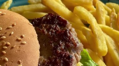 Marul, domates ve turşulu ızgara burger, deniz kenarındaki bir restoranda turkuaz bir tabakta altın cipsle servis edilir.
