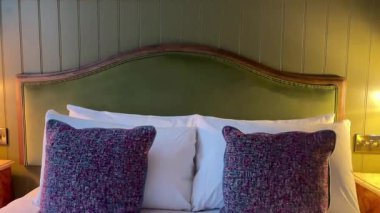 Ilık bir şekilde Londra 'daki otel odasında yeşil yatak başlığı, pelüş yastıklar ve zamansız İngiliz tarzında eski ahşap komodinlerle.