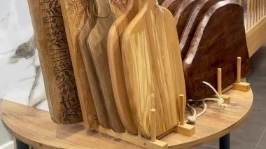 Çeşitli şekil ve tonlarda ahşap doğrama tahtalarının bir koleksiyonu bir ev eşyaları dükkanında güzelce sergileniyor, yavaş çekimde.
