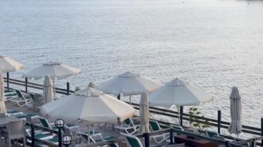 Şemsiyeler ve dinlenme yerleri, Türkiye 'nin Bodrum kenti yakınlarında sakin mavi dalgalara, yavaş çekime bakan huzurlu bir rıhtımda kuyruk oluşturuyorlar.